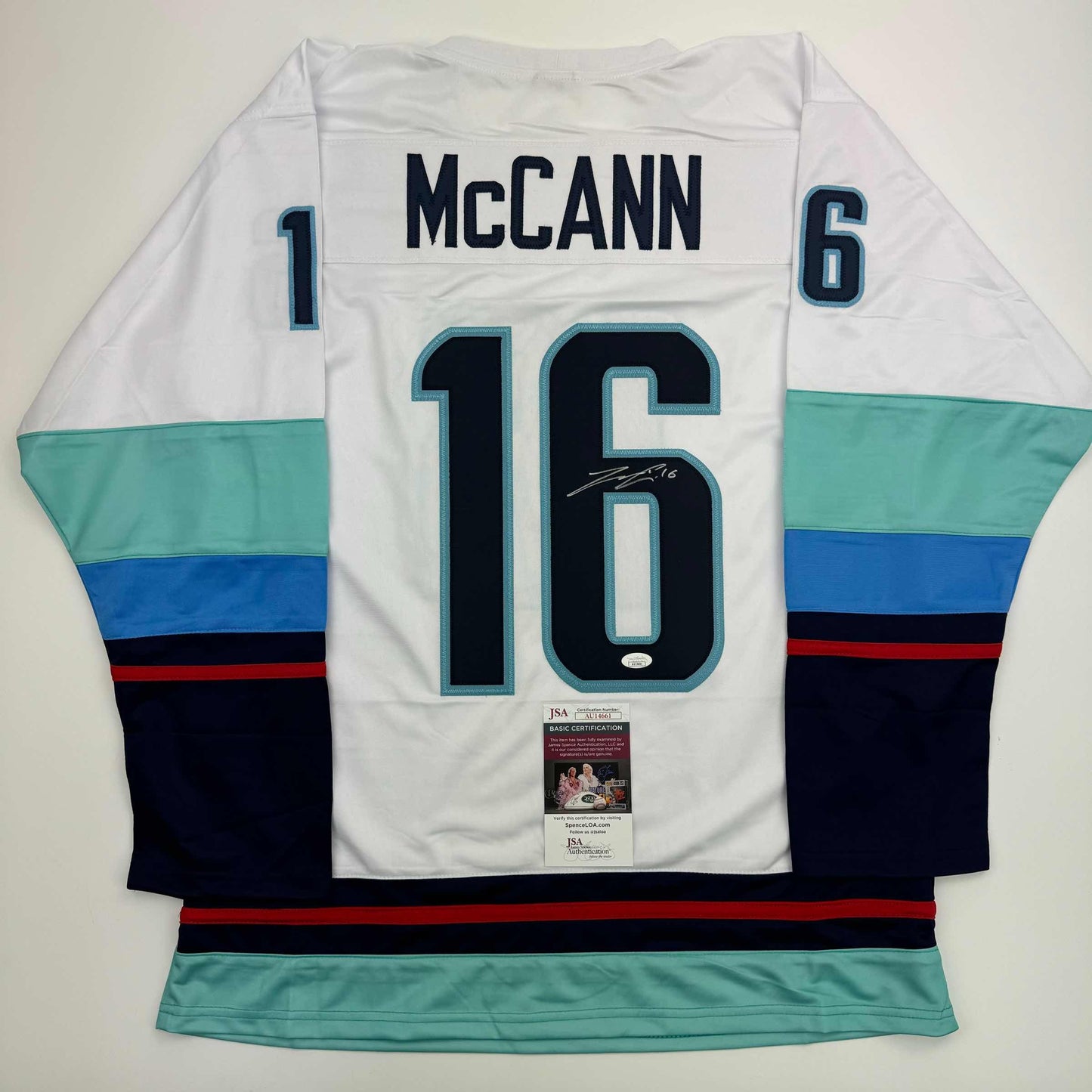 Rear view of white Jared McCann hockey jersey number 16 with teal and navy stripes, JSA authentication certificate visible.