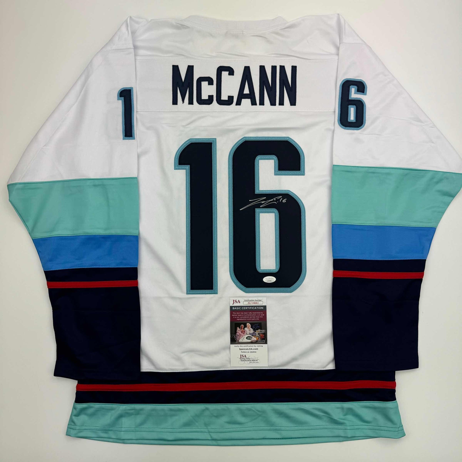 Rear view of white Jared McCann hockey jersey number 16 with teal and navy stripes, JSA authentication certificate visible.