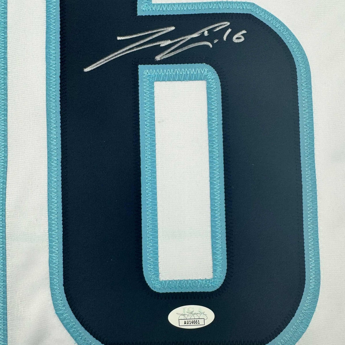 Close-up of navy hockey jersey back with turquoise trim, white number zero panel, silver signature reading "2016" and JSA authentication sticker.