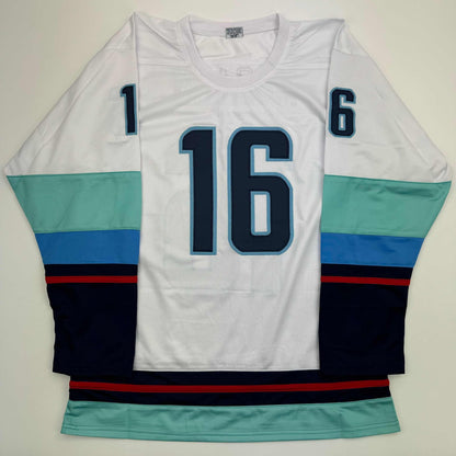 White hockey jersey number 16 with navy and light blue numbering, displayed flat showing front body and striped sleeves in teal, navy, and red.