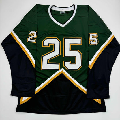 Flat lay of green and black hockey jersey with number 25 and gold/white trim displayed against white background.