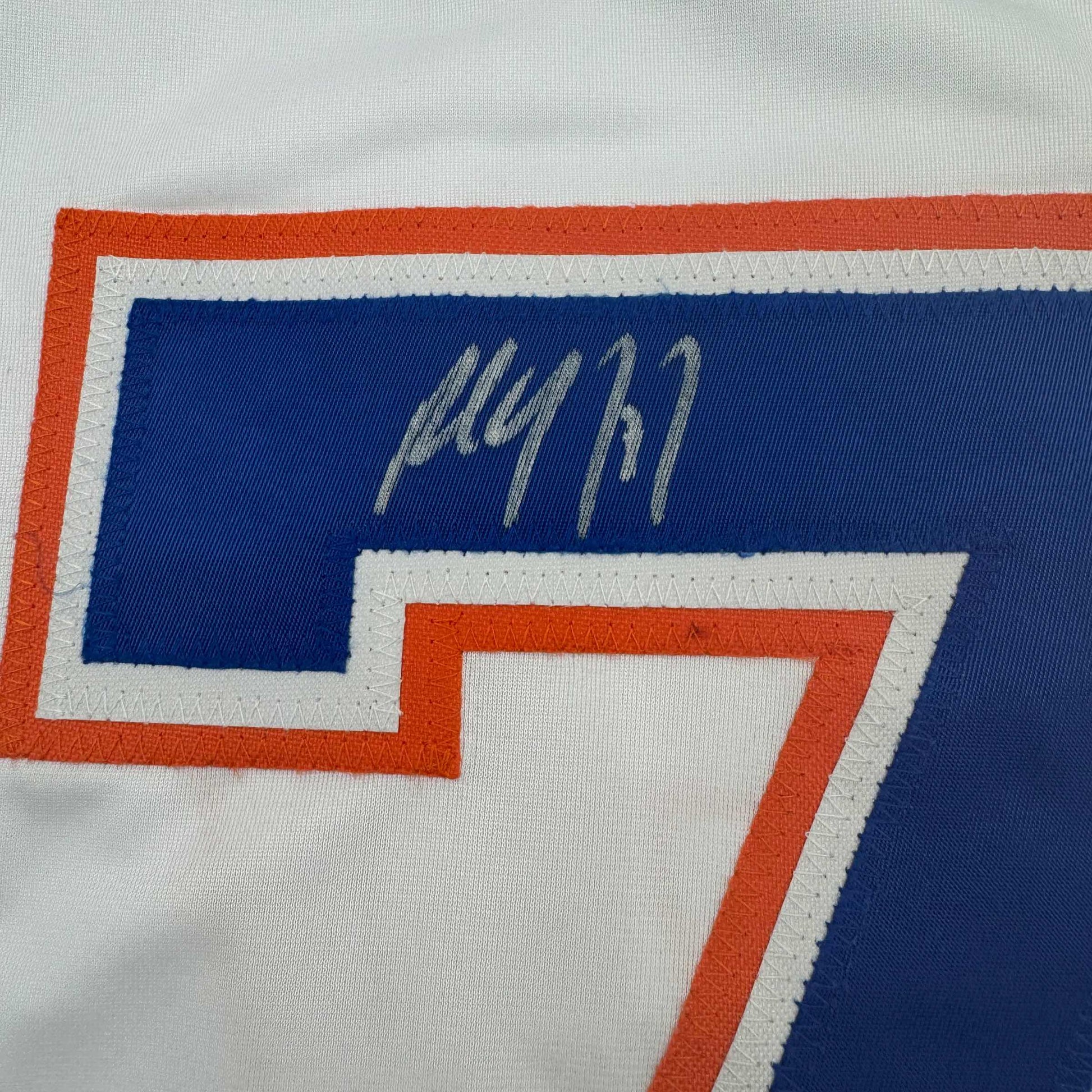Close-up of handwritten signature on blue panel of white Edmonton Oilers hockey jersey with orange and gray trim.