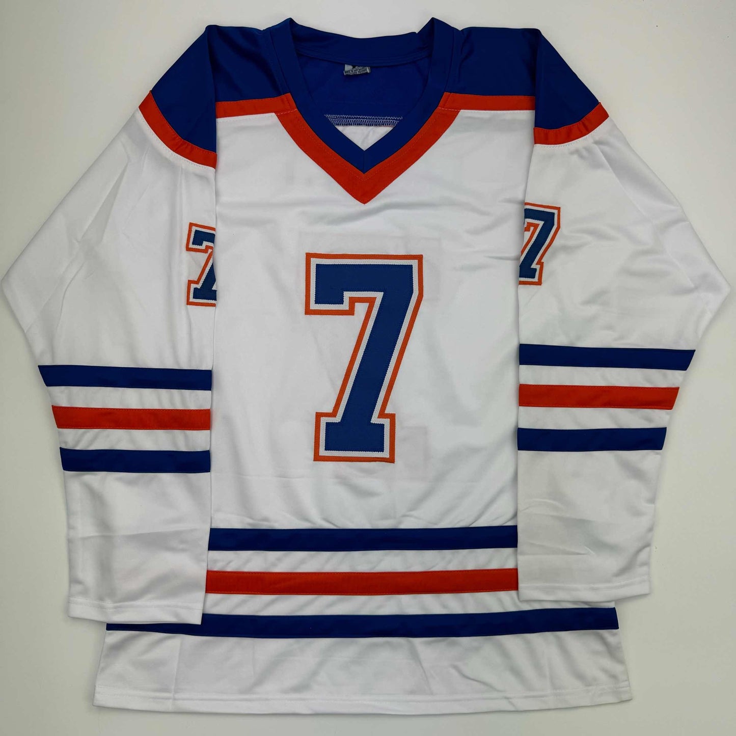 White Edmonton Oilers hockey jersey number 7 with navy blue and red trim, displayed flat against gray background.