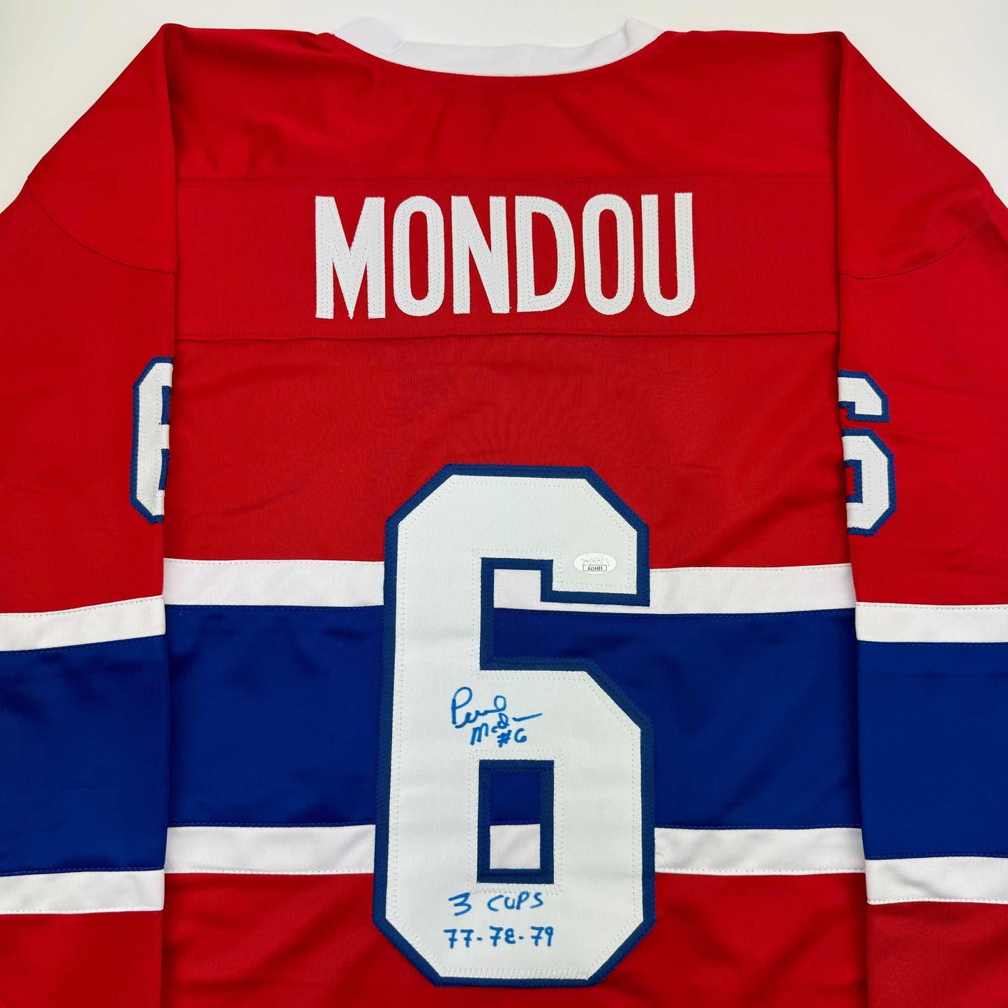 Back view of red, white, and blue Montreal Canadiens hockey jersey with "MONDOU" nameplate and number 6 with handwritten inscription.