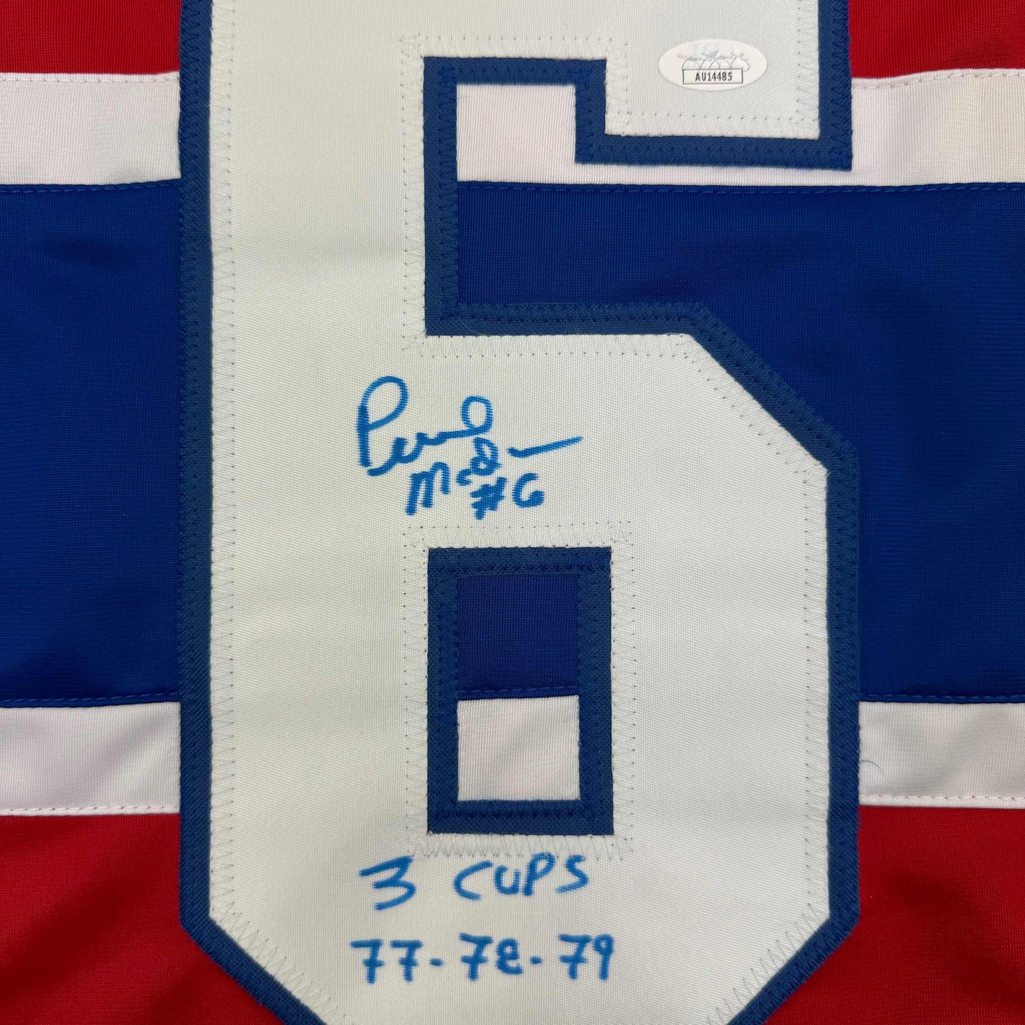 Close-up of autographed Montreal Canadiens hockey jersey number 6 with blue pen signature and "3 Cups 77-78-79" inscription.
