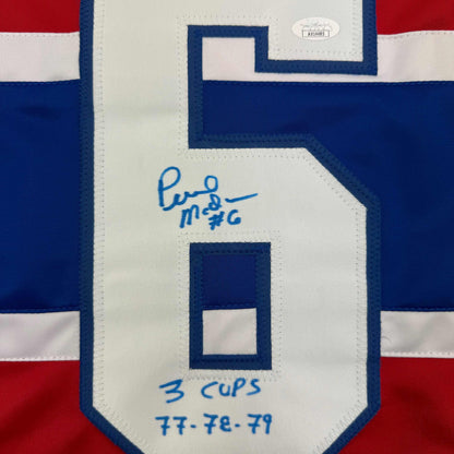 Close-up of autographed Montreal Canadiens hockey jersey number 6 with blue pen signature and "3 Cups 77-78-79" inscription.