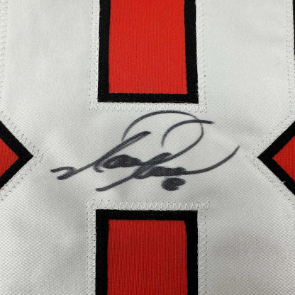 Close-up of autographed Mark Recchi jersey showing handwritten signature in black ink on white fabric with red and black geometric design elements.