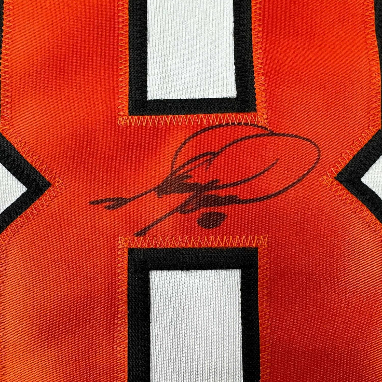 Close-up of autographed Mark Recchi orange Philadelphia Flyers jersey showing signed cursive signature on red fabric with black and white trim.