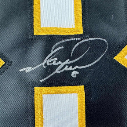 Close-up of autographed Mark Recchi signature in silver ink on black Pittsburgh Penguins jersey with yellow and white trim.