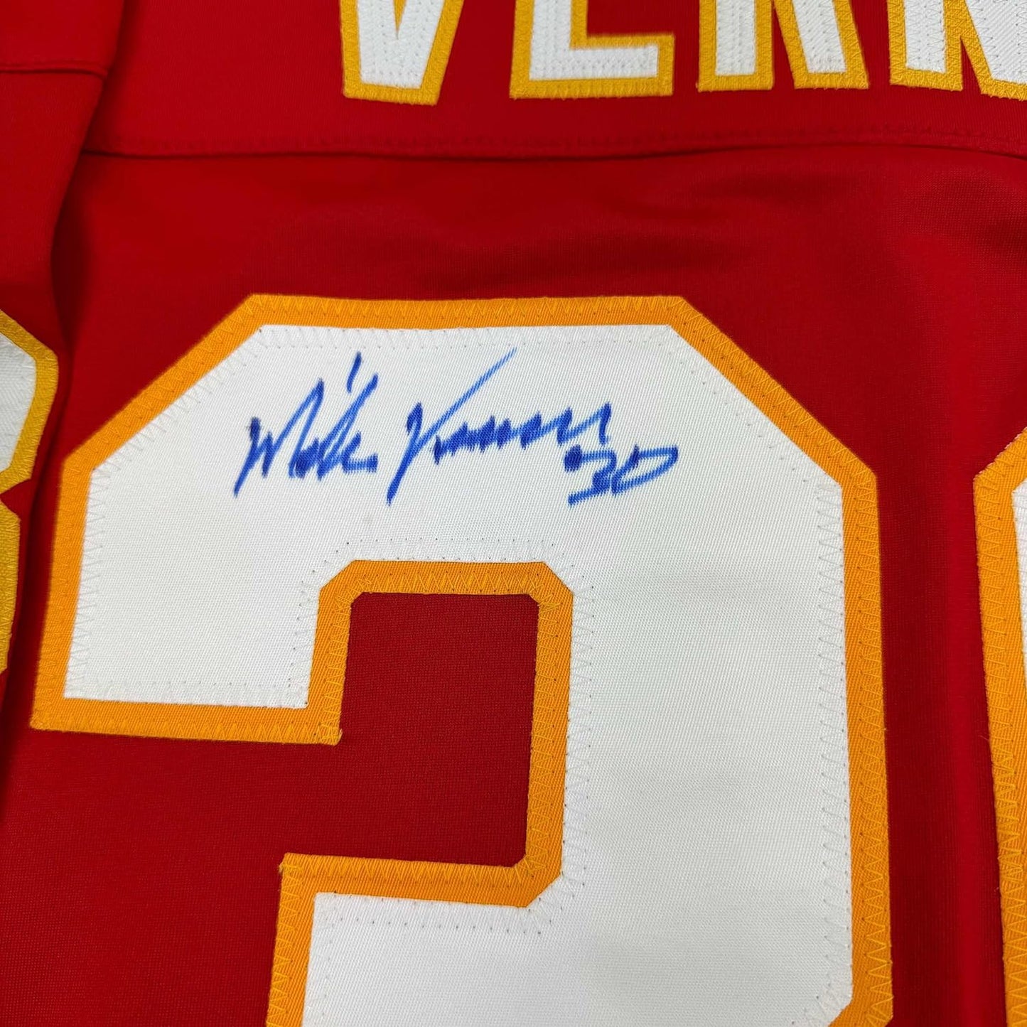 Close-up of signed white jersey number on red fabric with blue autograph and gold trim.
