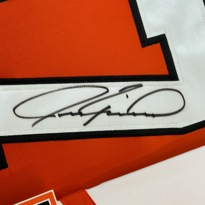 Close-up of handwritten signature on white stripe of orange and black hockey jersey.