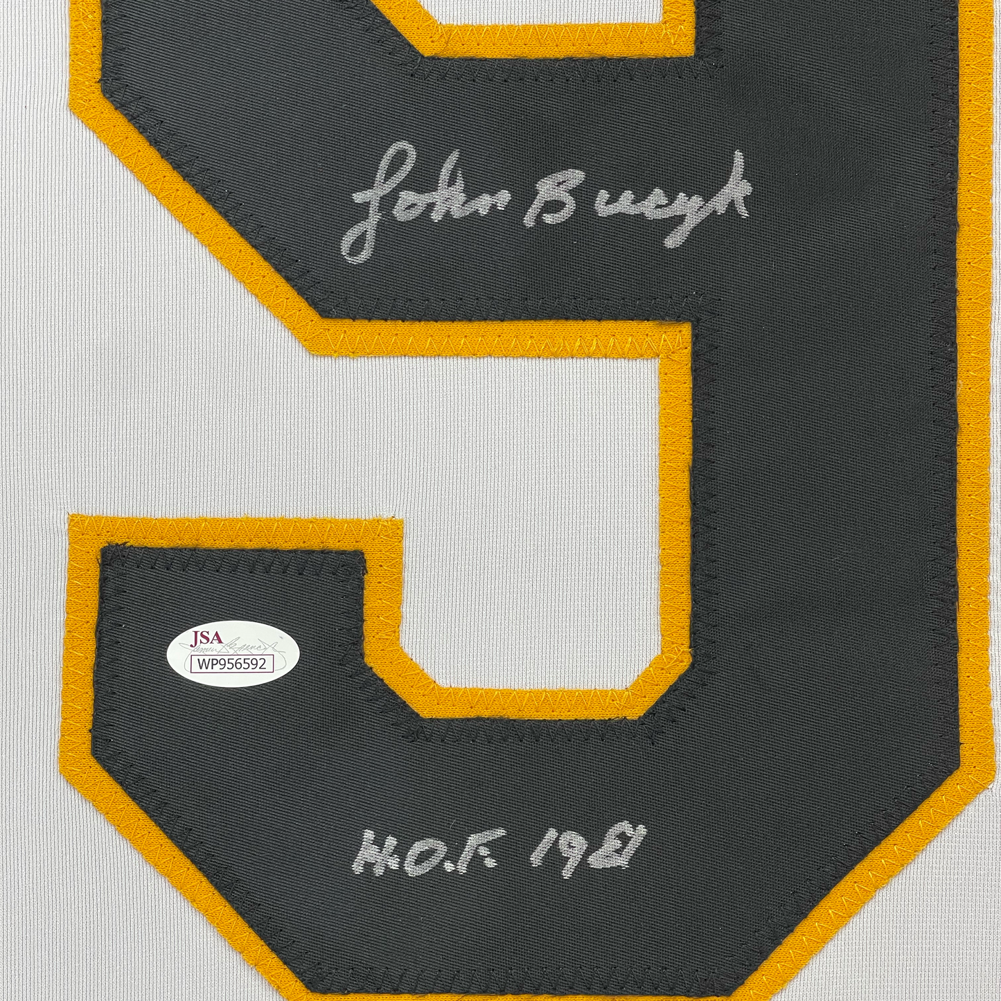 Close-up of dark gray hockey jersey back panel with gold trim, showing "John Bucyk" signature and "H.O.F 1981" text with JSA authentication sticker.