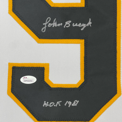 Close-up of dark gray hockey jersey back panel with gold trim, showing "John Bucyk" signature and "H.O.F 1981" text with JSA authentication sticker.