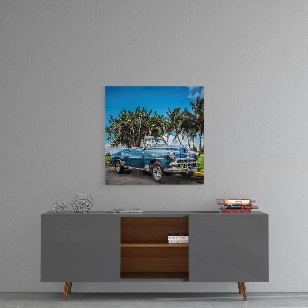 Blue vintage convertible car parked beneath palm trees against clear sky on square glass wall art.