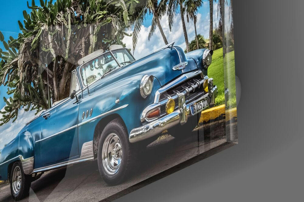 Blue vintage convertible car displayed on glass wall art with palm trees and green grass background.