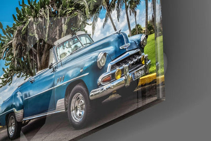 Blue vintage convertible car displayed on glass wall art with palm trees and green grass background.