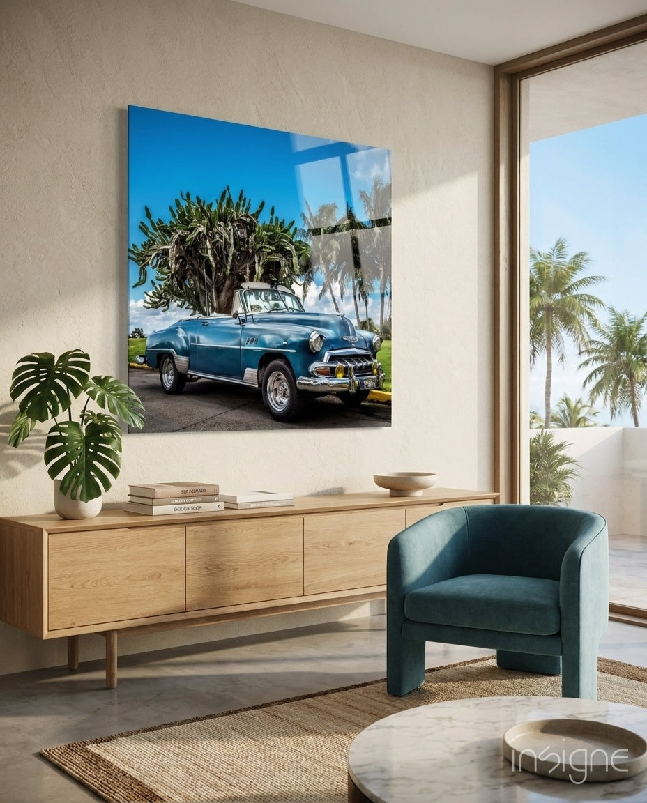Blue vintage convertible car with palm trees displayed as glass wall art above wooden sideboard in modern living room.