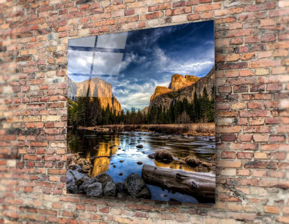 Glass wall art mounted on brick wall displaying a river valley landscape with golden cliffs, pine forests, and blue sky.
