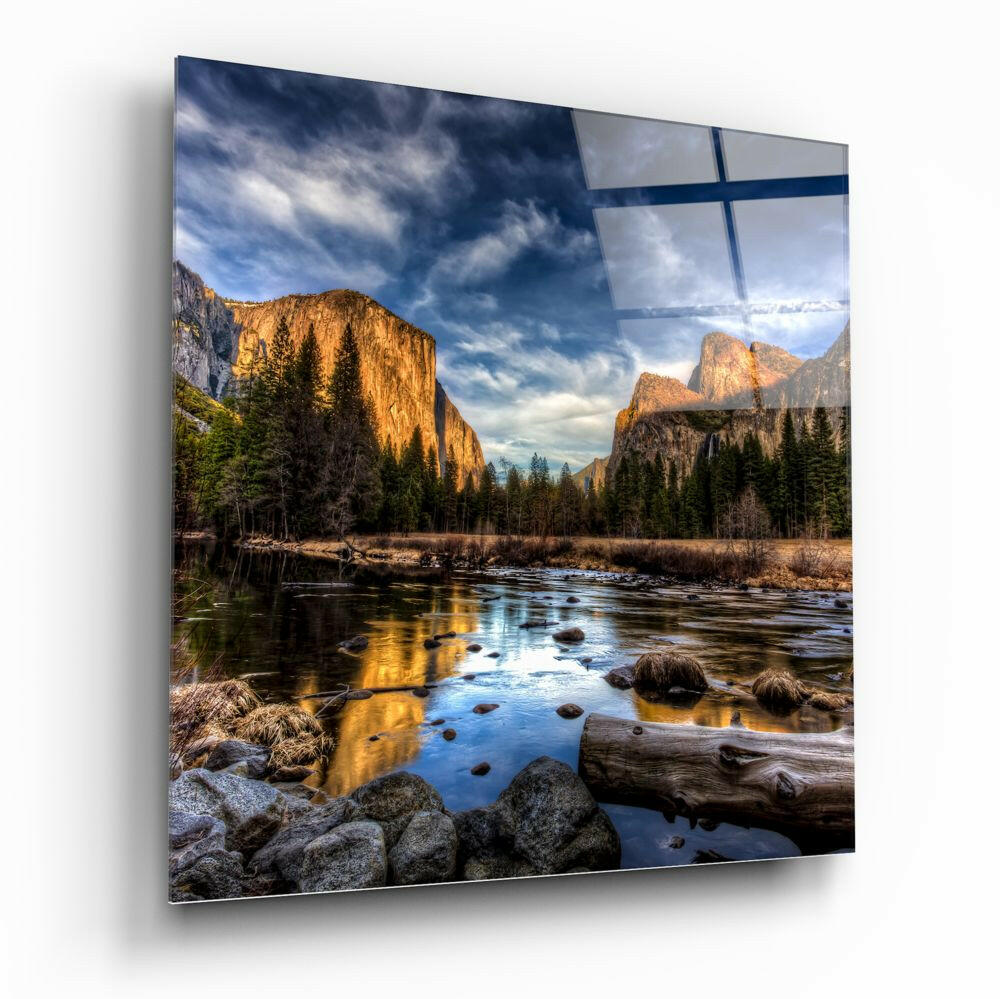 Glass wall panel displaying a mountain valley landscape with a river, evergreen trees, golden cliffs, and blue sky reflected in the glossy surface.