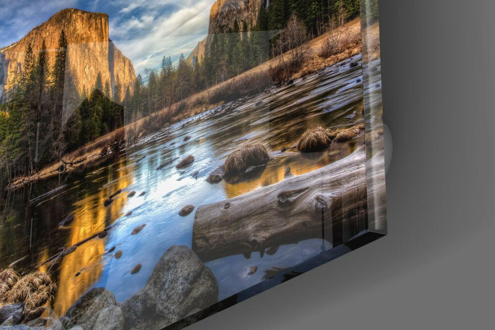 Mountain river with golden cliff reflection, fallen logs, and evergreen forest on glass wall art panel.