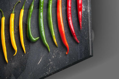 Nine chili peppers in yellow, green, orange, and red arranged in a gradient row on a dark textured surface.