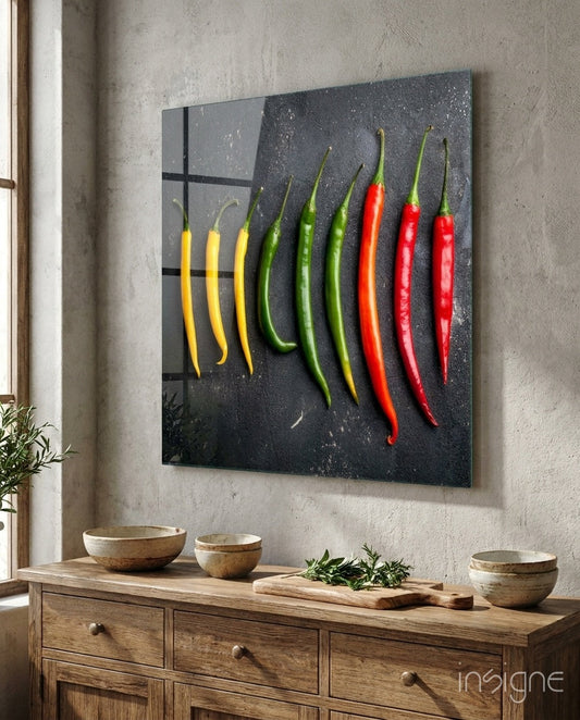 Glass wall art displaying a gradient of colored chili peppers from yellow to red, mounted above a wooden dresser in a minimalist kitchen setting.