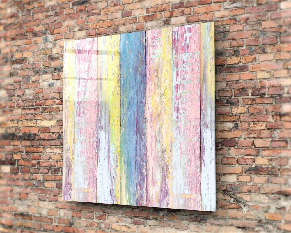 Colorful wooden patterned glass wall art with vertical pink, yellow, blue, and white stripes mounted on a brick wall.