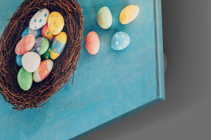 Overhead view of colorful hand-painted Easter eggs in a brown woven nest on turquoise background, with additional eggs scattered beside it.