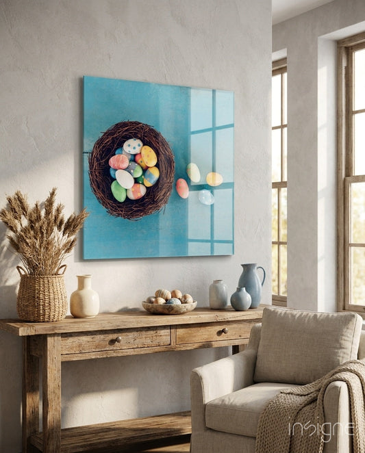 Blue glass wall art featuring a dark woven nest with colorful Easter eggs displayed above a wooden console table in a bright room.