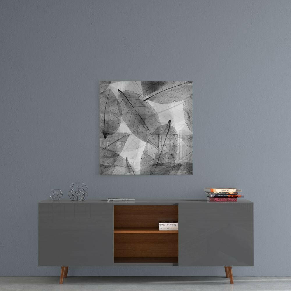Black and white glass wall art with translucent overlapping leaves hanging above a gray mid-century modern credenza with wooden center shelf.
