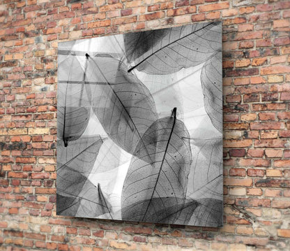 Black and white glass wall art featuring overlapping skeletal leaf designs mounted on a red brick wall.
