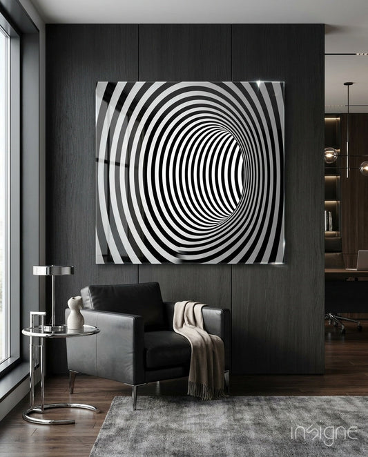 Black and white concentric striped tunnel illusion artwork displayed on dark textured wall above grey leather chair in modern interior.