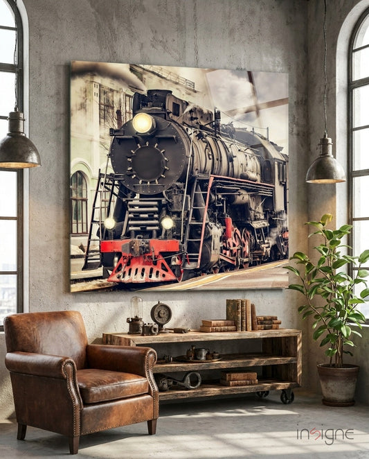 Vintage steam locomotive glass art displayed on industrial concrete wall above leather chair and wooden desk in loft setting.