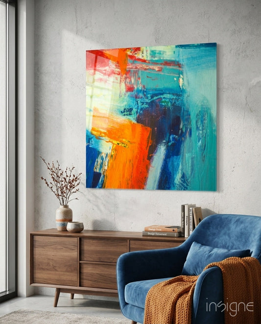 Vibrant orange, blue, and teal abstract glass art panel displayed on concrete wall above wooden dresser in modern living room setting.