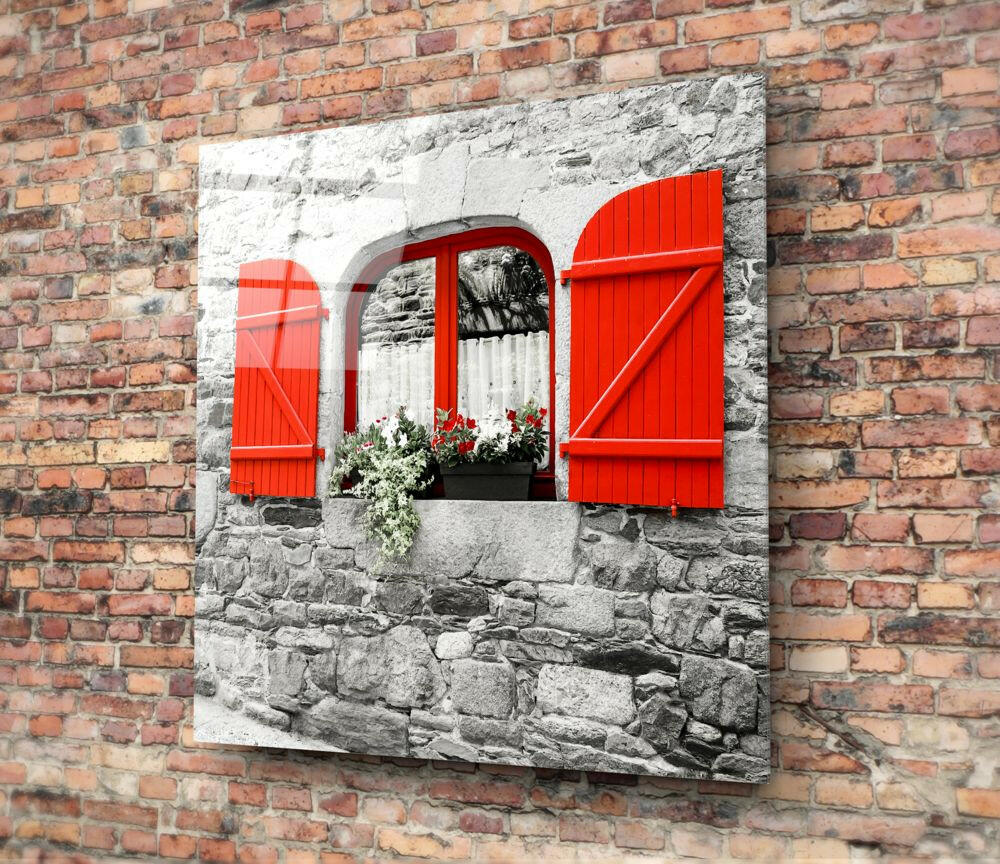 Red Window Glass Wall Art mounted on brick wall, displaying black-and-white stone cottage with vibrant red shutters and flower box.