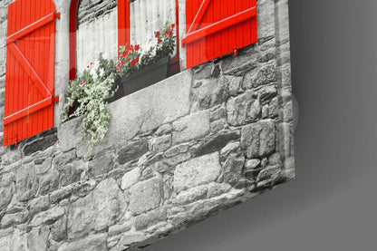 Bright red shutters and window box on weathered gray stone wall with cascading green and pink flowers.