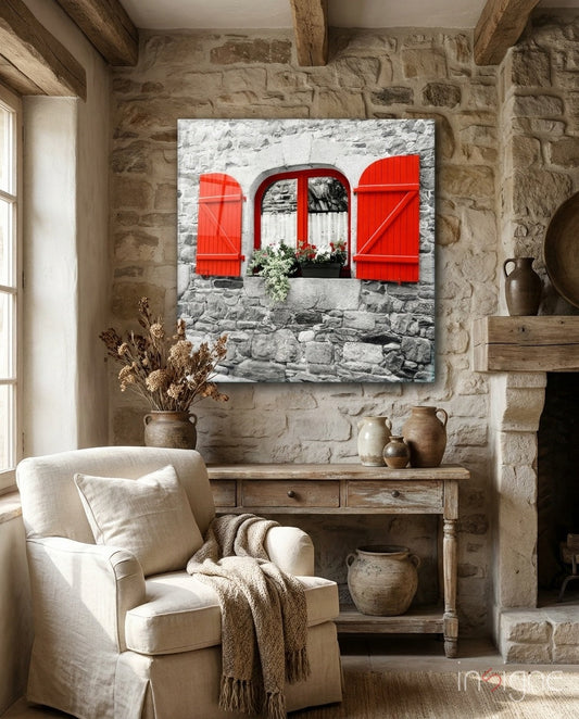 Red shutters and window with flowering box on stone wall displayed above wooden console table in rustic interior.