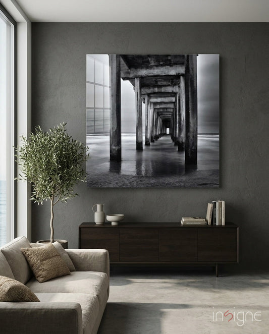 Black and white photograph of pier arches receding into distance, displayed as framed glass wall art above dark wooden credenza in modern living room.