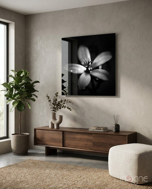 Black and white backlit flower artwork mounted above wooden console in minimalist room with plants and cream pouf.