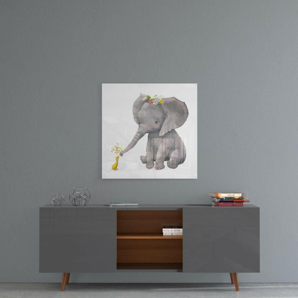 Square glass wall art depicting a gray elephant with flower crown offering flowers to a small yellow duck, displayed above a mid-century modern console table.