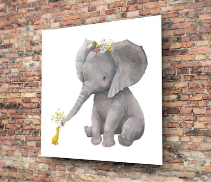 Glass wall art mounted on brick wall showing watercolor illustration of gray elephant with flower crown and small yellow duck holding flowers.