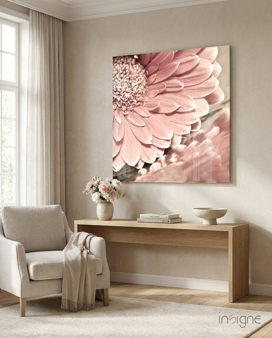 Soft pink gerbera daisy glass art hanging above wooden console table in neutral bedroom with chair and flowers.
