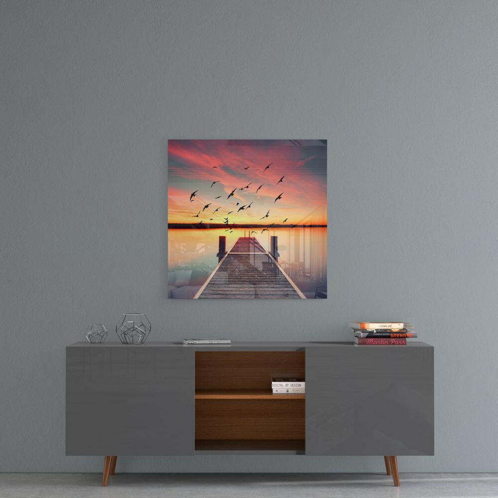 Red Dock glass wall art hanging above a gray console table, displaying a wooden pier at sunset with flying birds and pink-orange sky.