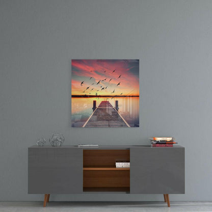 Red Dock glass wall art hanging above a gray console table, displaying a wooden pier at sunset with flying birds and pink-orange sky.