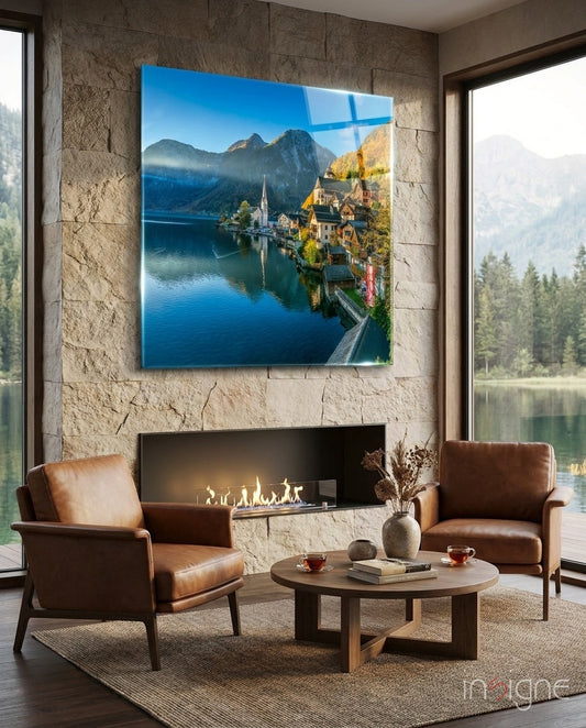 Hallstatt Glass Wall Art depicting Alpine lake village with church spire, mountains, and blue water, displayed above fireplace in modern living room.