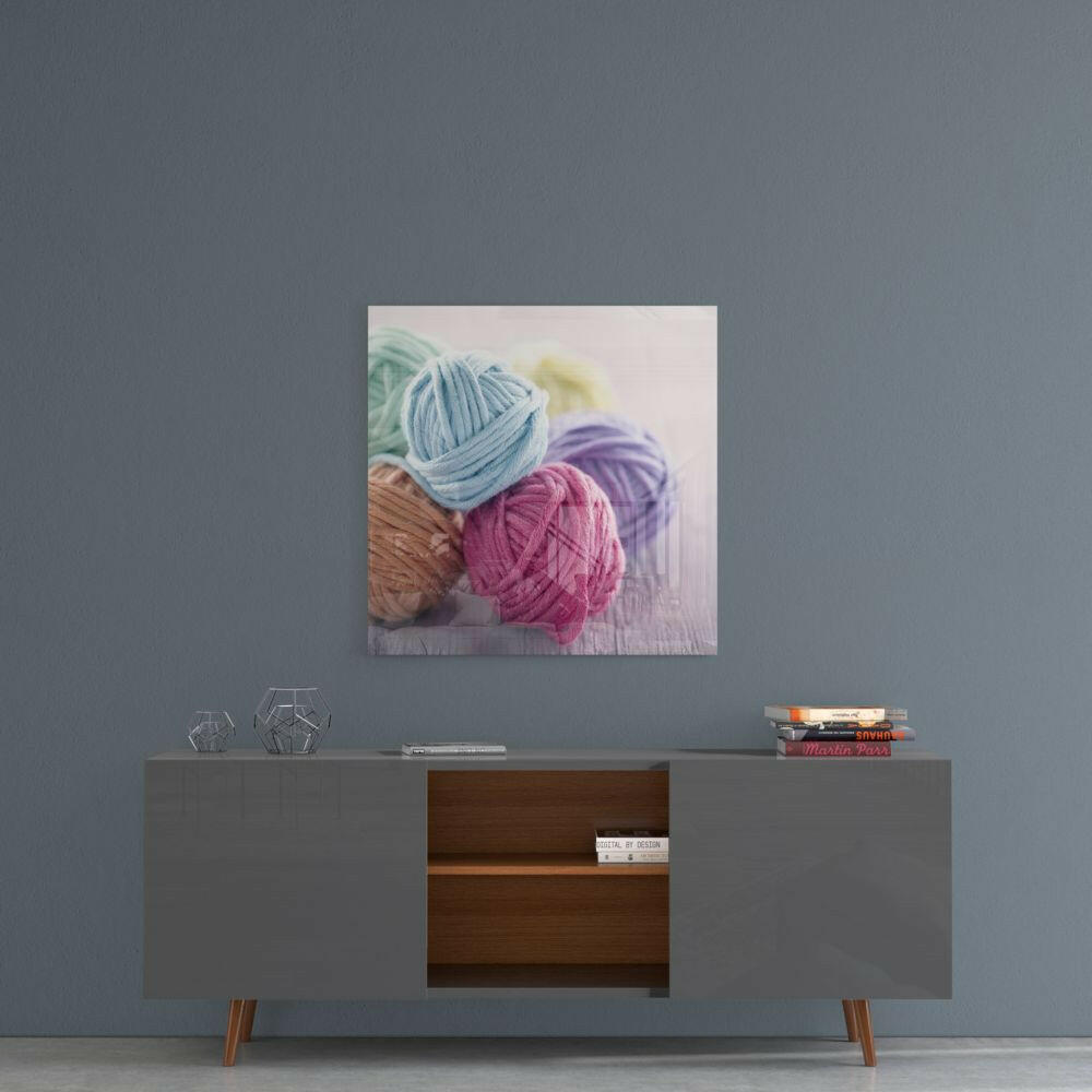 Colored yarn balls in blue, pink, purple, and brown displayed on glass wall art hanging above a mid-century modern console table.