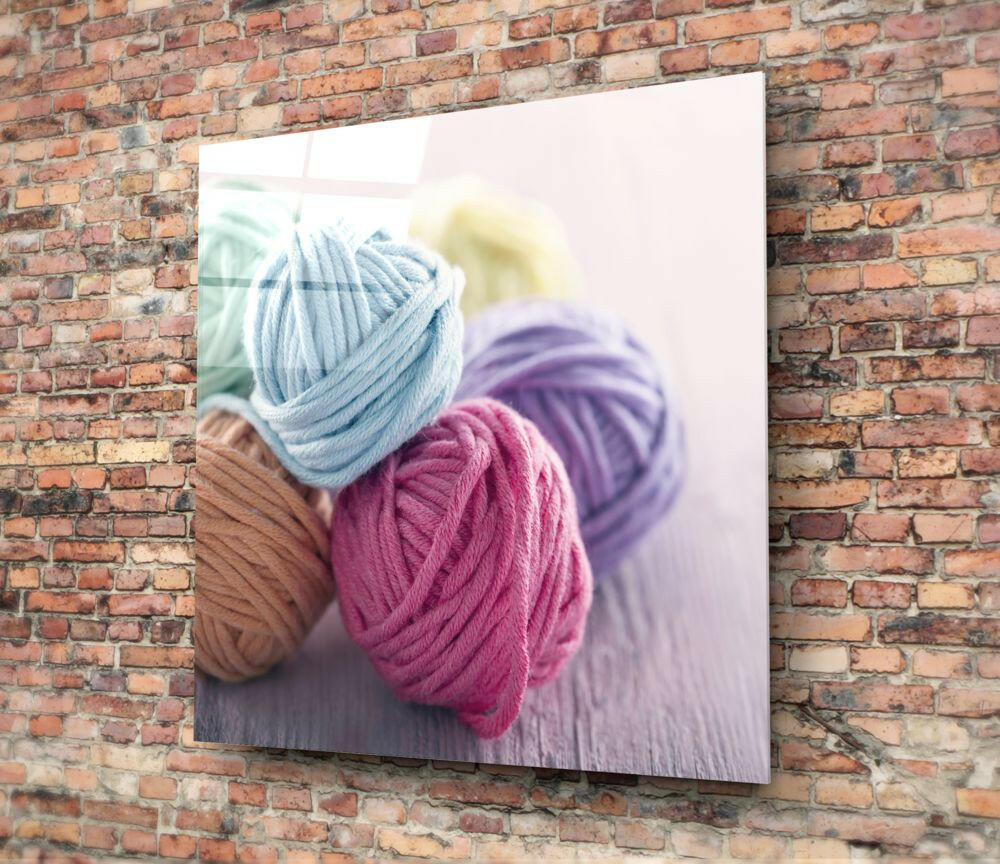 Colorful yarn balls in blue, pink, and purple displayed on glass wall art mounted on red brick.