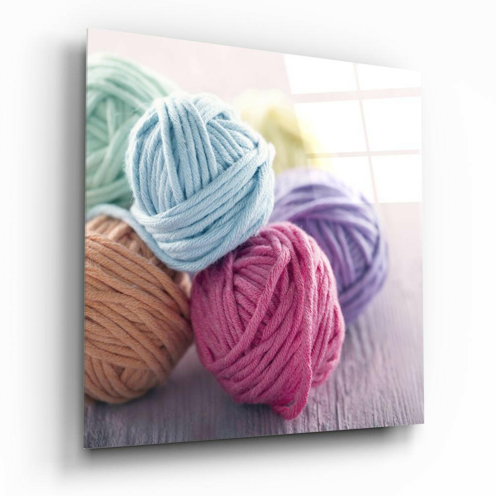 Colorful yarn balls in blue, pink, purple, tan, and green arranged on a wooden surface with a bright window in the background.