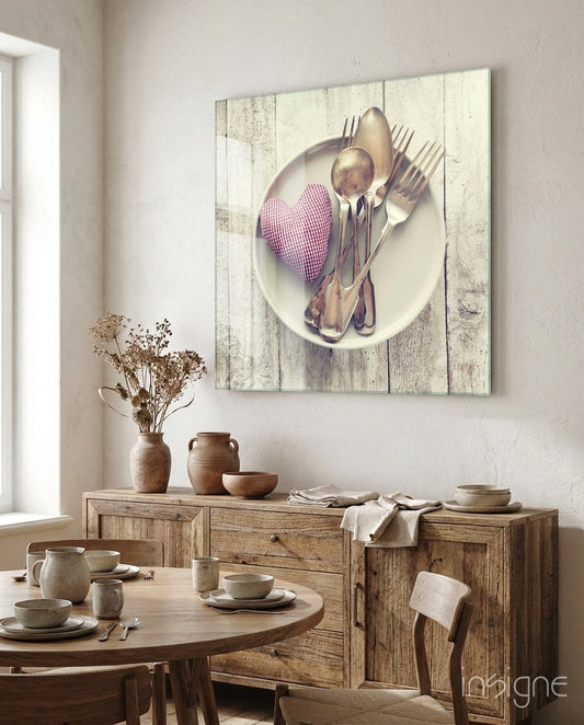 Glass wall art featuring silver cutlery and pink gingham heart on white wooden plank background, displayed in rustic dining room setting.