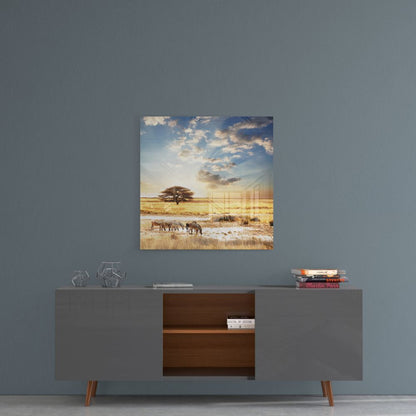 Glass wall art depicting African savanna landscape with acacia tree, elephants, golden grassland, and dramatic sky displayed above gray sideboard.